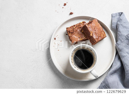 Pieces of chocolate brownie with nuts on a plate with a cup of espresso coffee on a light background 122679629