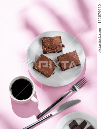 Pieces of chocolate brownie with nuts on a plate with a cup of espresso coffee on a pink background 122679630