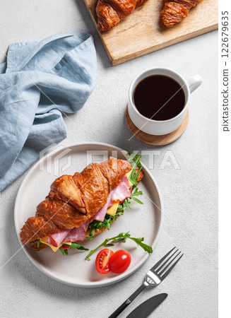 Croissant sandwich with ham, cheese, tomato  and arugula on a plate on a light background 122679635