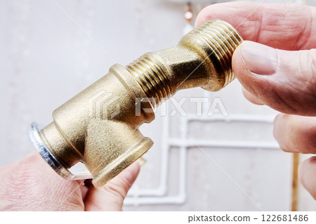 Dog legs reducer, brass plumbing fitting held in hands, ready for installation. Dog legs reducer, brass plumbing fitting held in hands, ready for installation. 122681486