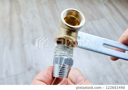 Plumbing flax is wrapped around stainless steel threaded reducer nipple, preparing it for installation into brass pipe fitting. Plumbing flax is wrapped around stainless steel threaded reducer nipple, preparing it for installation into brass pipe fitting. 122681498