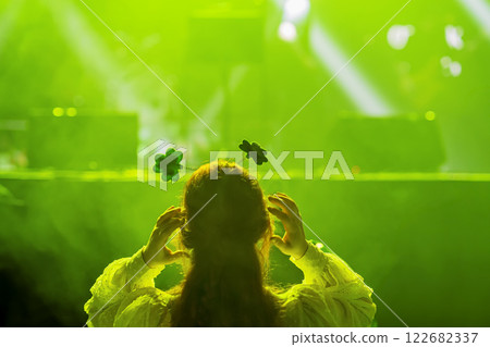 Woman with clover-themed headband in front of green glowing stage, St. Patrick's Day celebration. Concept of Irish culture, luck, festive spirit Woman with clover-themed headband in front of green glowing stage, St. Patrick's Day celebration. Concept of Irish culture, luck, festive spirit 122682337