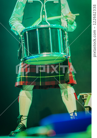 Holiday of St. Patrick's Day, music. Scottish drummer with traditional kilt performing live on stage close-up. Drumsticks in hand, vibrant stage Holiday of St. Patrick's Day, music. Scottish drummer with traditional kilt performing live on stage close-up. Drumsticks in hand, vibrant stage 122682338