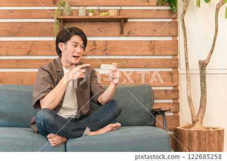 Young Asian man relaxing in the living room at home looking at his smartphone (surprised, shocked, shocked, astonished) Young Asian man relaxing in the living room at home looking at his smartphone (surprised, shocked, shocked, astonished) 122685258