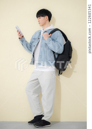 Full body of a boy carrying a backpack and holding a smartphone, spring-like yellow background 122685341