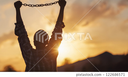 希望和勝利，在耀眼的夕陽下，一個男人緊緊抓住斷掉的鎖鏈的側影 122686571