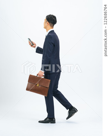 一位中年男性商務人士拿著智慧型手機行走的全身照片 122686764