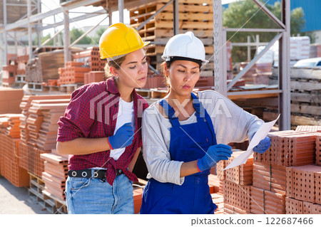 Two female storekeepers are discussing work issues in the warehouse, holding an estimate in their hands Two female storekeepers are discussing work issues in the warehouse, holding an estimate in their hands 122687466