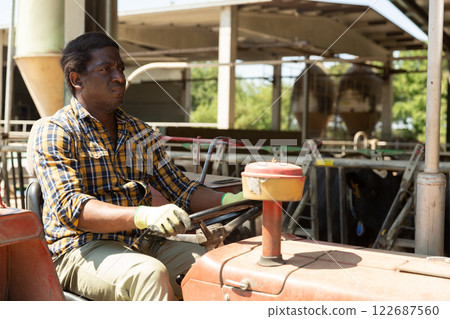 Man driving farm tractor during spring works on cowshed Man driving farm tractor during spring works on cowshed 122687560
