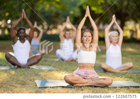 Group of people of different ages and nationalities doing yoga together in park - lotus pose 122687575