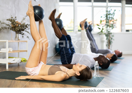 Young woman doing exercises with pilates ball during group workout 122687603
