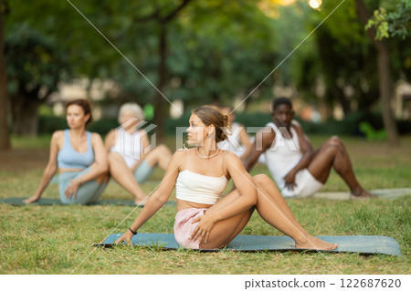 Girl performing Vakrasana during group yoga session outdoors 122687620