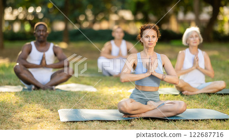 Woman meditating in lotus position at group yoga class in park Woman meditating in lotus position at group yoga class in park 122687716