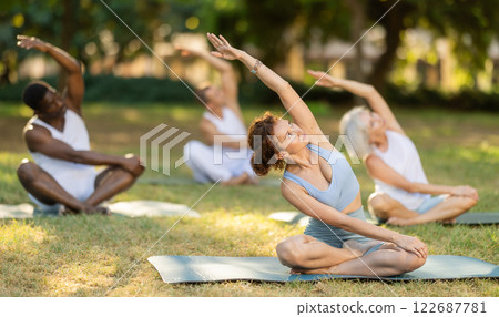 Woman stretching in lotus position during group yoga in park 122687781