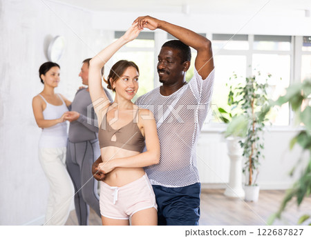 Young woman and African American man dancing ballroom dances in pair Young woman and African American man dancing ballroom dances in pair 122687827