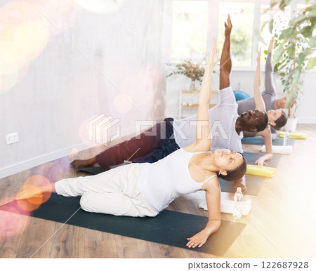 Young girl with multinational group of active people doing stretching exercises during yoga class 122687928