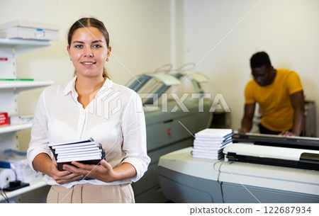 Portrait of happy young female specialist holding printed samples of notebooks in the print shop 122687934