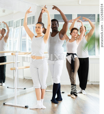 Ballet troupe stand in fifth position near ballet barre during group training in dance studio Ballet troupe stand in fifth position near ballet barre during group training in dance studio 122688034
