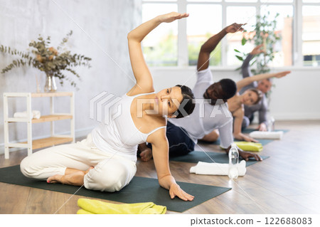 Young girl with multinational group of active people doing stretching exercises during yoga class 122688083