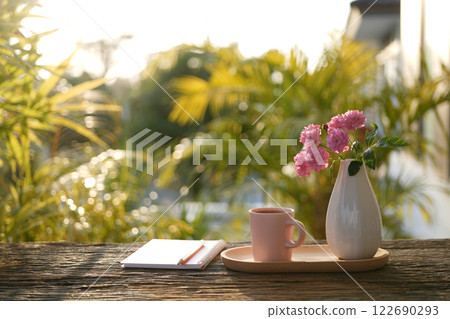 Pink ceramic coffee cup and a white vase of rose flowers and notebooks 122690293