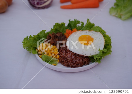 A vibrant meal consisting of red rice, meat, corn, carrots, lettuce, omelet and a sunny side 122690791