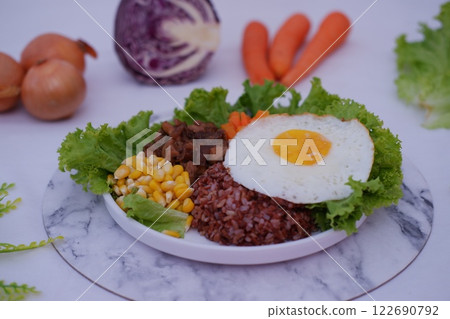 A vibrant meal consisting of red rice, meat, corn, carrots, lettuce, omelet and a sunny side 122690792