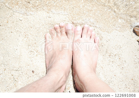 Woman's and men's feet on the sand at the beach in the summer. Woman's and men's feet on the sand at the beach in the summer. 122691008
