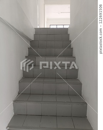 A Staircase leading to bright room with white walls and tiled steps A Staircase leading to bright room with white walls and tiled steps 122691506