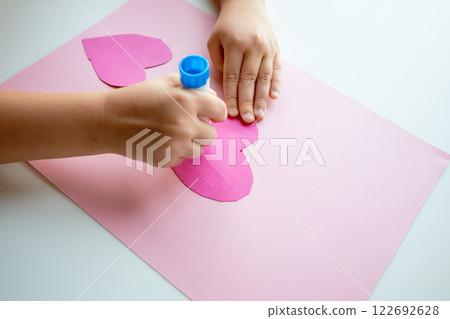 Child making heart shaped craft with pink paper and glue stick Child making heart shaped craft with pink paper and glue stick 122692628