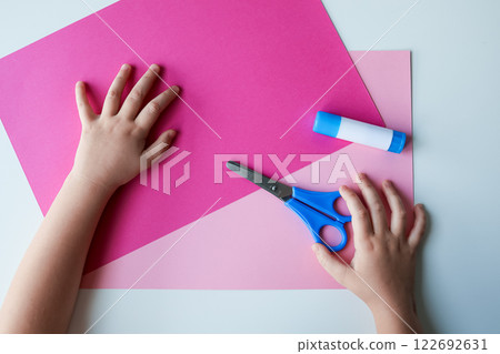 Child handcrafting with pink paper, scissors, and glue Child handcrafting with pink paper, scissors, and glue 122692631