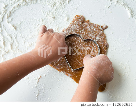Child making heart shaped cookie with dough and cutter on floured surface 122692635