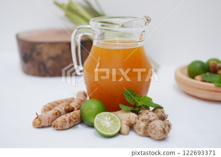Fresh ginger and lemon juice in a glass jar with ginger roots on white background. Fresh ginger and lemon juice in a glass jar with ginger roots on white background. 122693371