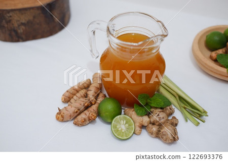 Fresh ginger and lemon juice in a glass jar with ginger roots on white background. Fresh ginger and lemon juice in a glass jar with ginger roots on white background. 122693376