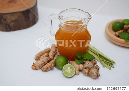 Fresh ginger and lemon juice in a glass jar with ginger roots on white background. Fresh ginger and lemon juice in a glass jar with ginger roots on white background. 122693377