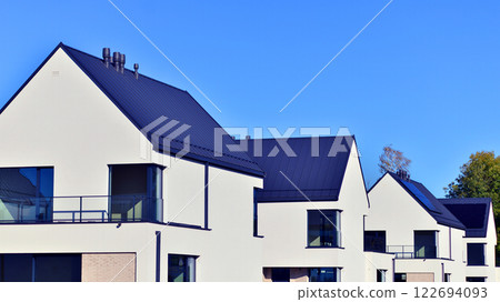Terraced family homes in newly developed housing estate. The real estate market in the suburbs. New single family houses in a new development area. Residential homes with modern facade.  122694093
