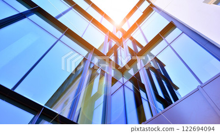 Glass building with transparent facade of the building and blue sky. Structural glass wall reflecting blue sky. Abstract modern architecture fragment. Contemporary architectural background. 122694094