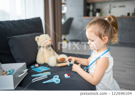 Little girl playing doctor with toys and teddy bear on the sofa in living room at home 122696104