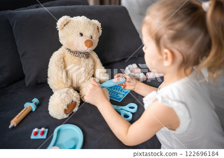 Little girl playing doctor with toys and teddy bear on the sofa in living room at home 122696184