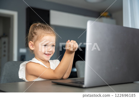 Little girl does finger gymnastics online on the laptop home. Distance learning concept. 122696185