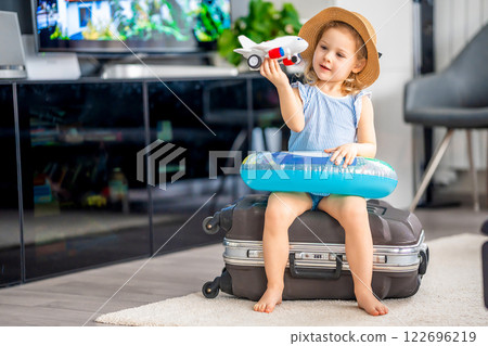 Little girl with suitcase baggage luggage and inflatable life buoy playing with toy plane and ready to go for traveling on vacation Little girl with suitcase baggage luggage and inflatable life buoy playing with toy plane and ready to go for traveling on vacation 122696219