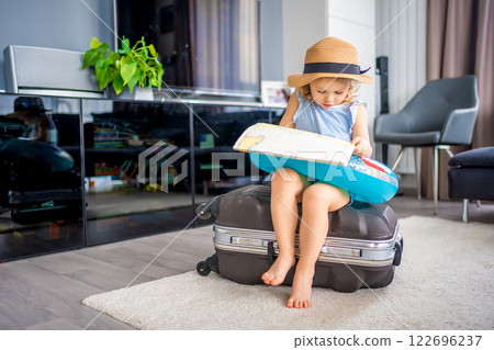 Little girl with suitcase baggage luggage and inflatable life buoy reading map and ready to go for traveling on vacation Little girl with suitcase baggage luggage and inflatable life buoy reading map and ready to go for traveling on vacation 122696237