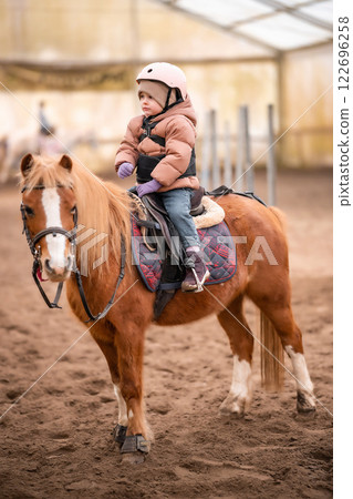 Little Child Riding Lesson. Three-year-old girl rides a pony and does exercises Little Child Riding Lesson. Three-year-old girl rides a pony and does exercises 122696258