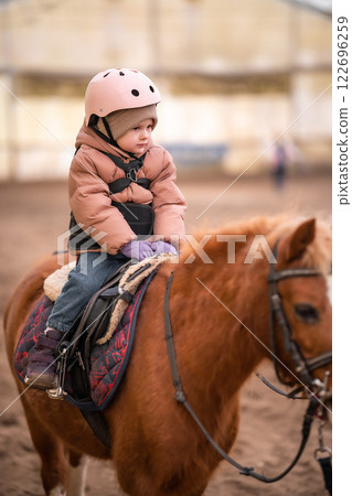 Little Child Riding Lesson. Three-year-old girl rides a pony and does exercises Little Child Riding Lesson. Three-year-old girl rides a pony and does exercises 122696259