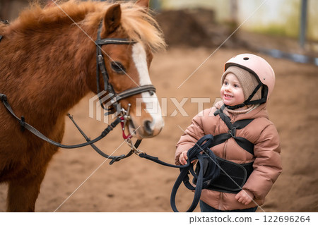 Portrait of little girl in protective jacket and helmet with her brown pony before riding Lesson 122696264