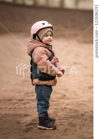 Portrait of little girl in protective jacket and helmet before riding lesson 122696291
