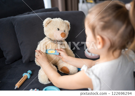 Little girl playing doctor with toys and teddy bear on the sofa in living room at home 122696294