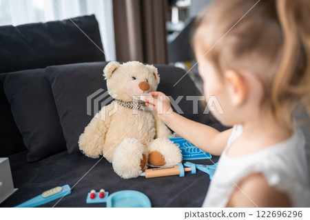 Little girl playing doctor with toys and teddy bear on the sofa in living room at home 122696296