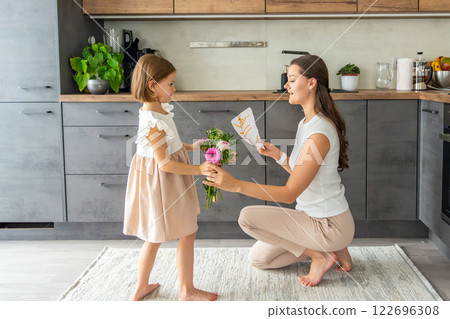 Little girl giving bouquet of flowers and drawing to her mum on the home kitchen. Mothers day, birthday or International Women's Day 8 march concept 122696308