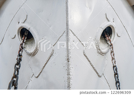 Ship's bow with anchor chains extending from the hawse holes, featuring weathered metal and welded seams detailed close view 122696309
