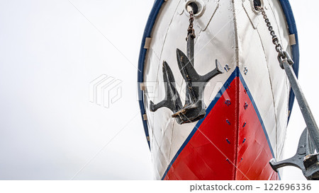 Ship's bow with a red and white hull, flanked by two large anchors on chains close-up. Vessel is docked on dry land for maintenance Ship's bow with a red and white hull, flanked by two large anchors on chains close-up. Vessel is docked on dry land for maintenance 122696336